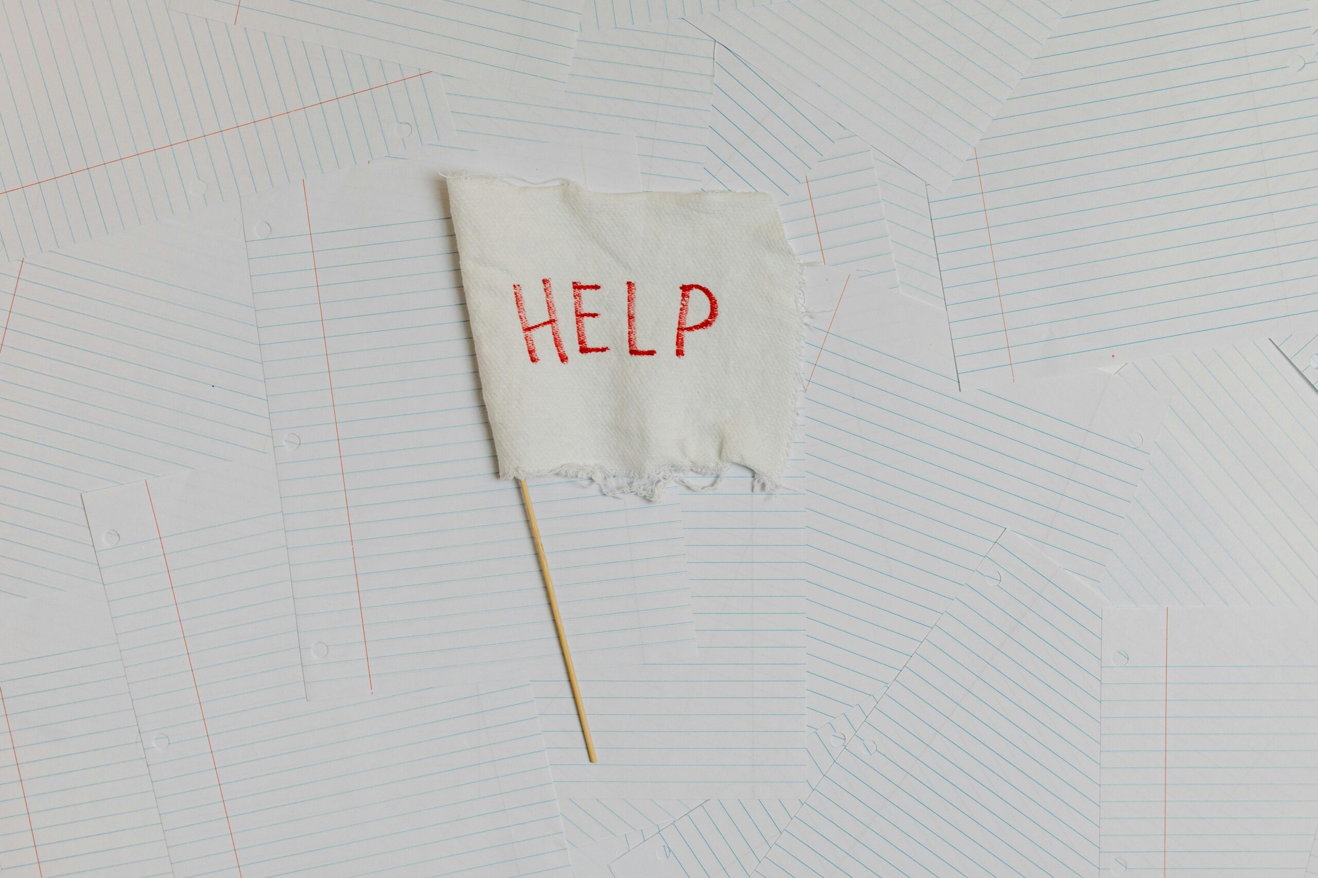 A fabric flag with 'HELP' on a scattered notepaper background, symbolizing distress or overwhelm.