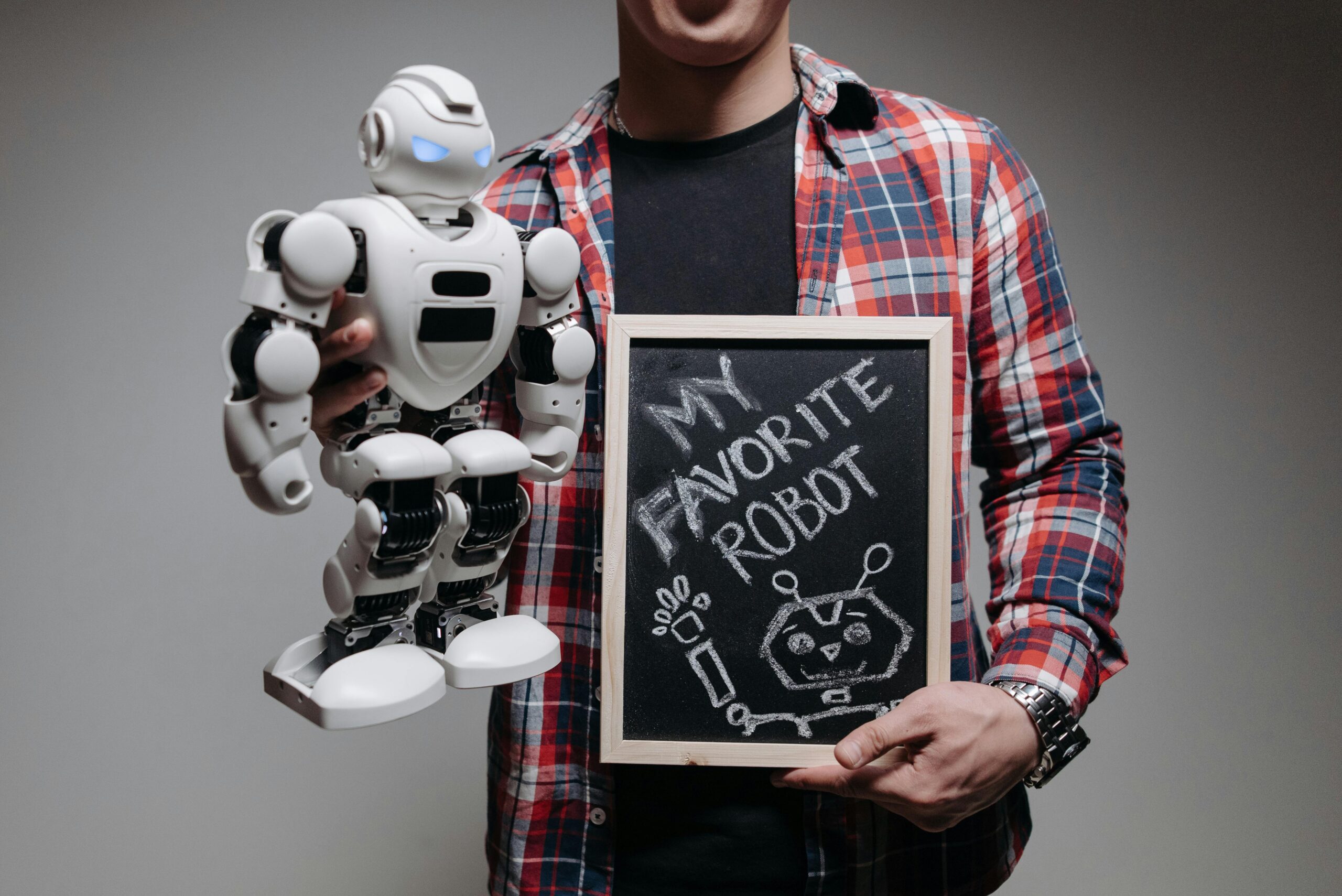A person holding a white robot and a chalkboard with 'My Favorite Robot' written on it in a studio setting.
