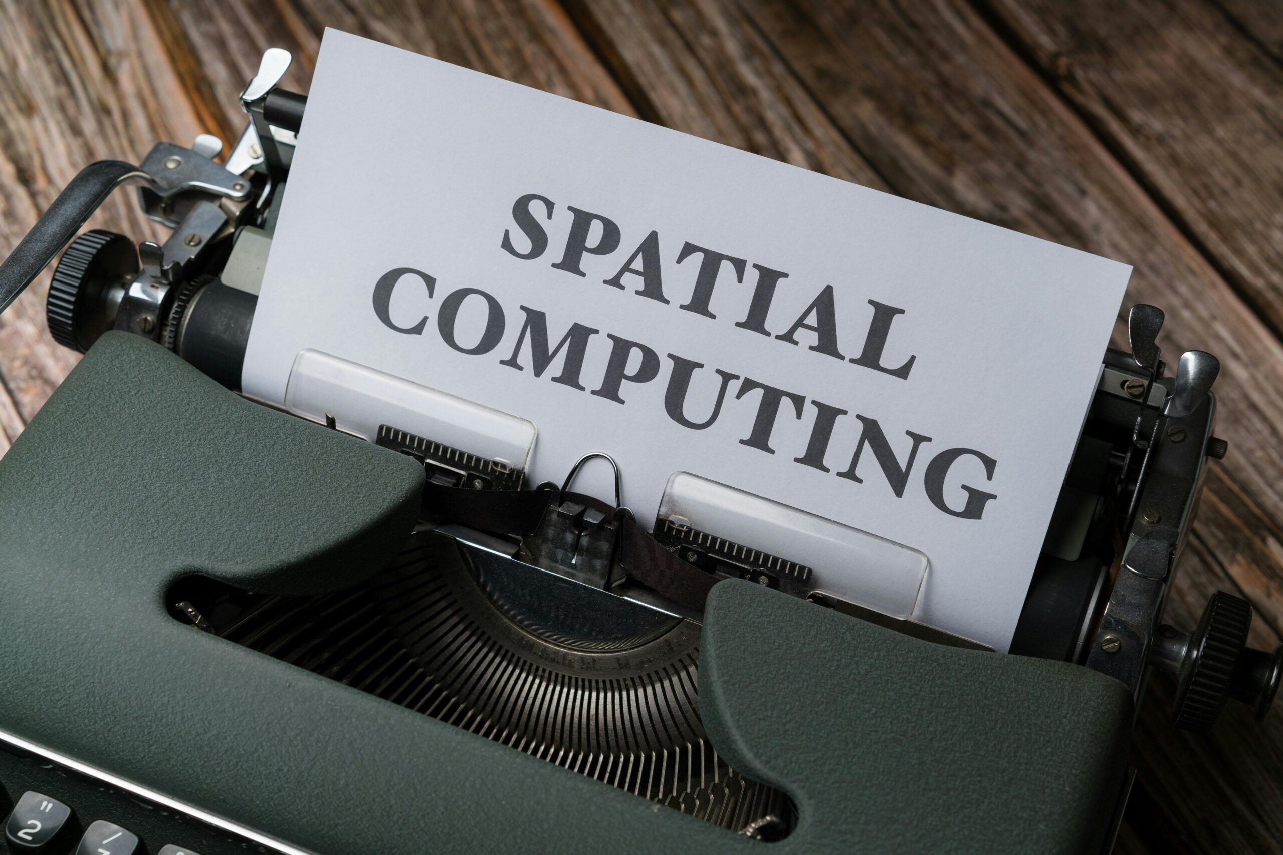A vintage typewriter with a paper displaying the text 'SPATIAL COMPUTING' on a wooden desk.