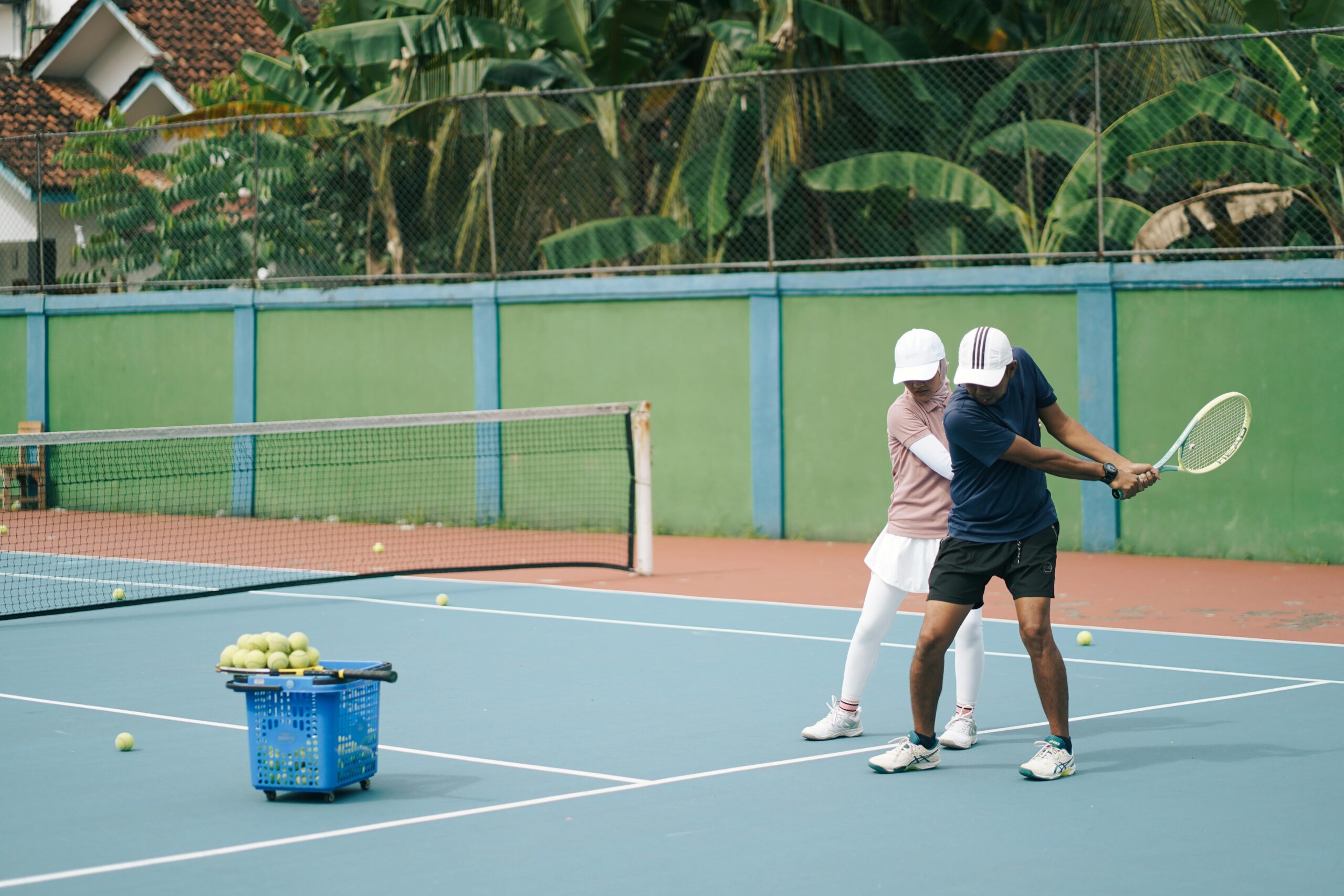 A tennis lesson in progress with a coach instructing a player on a sunny outdoor court.