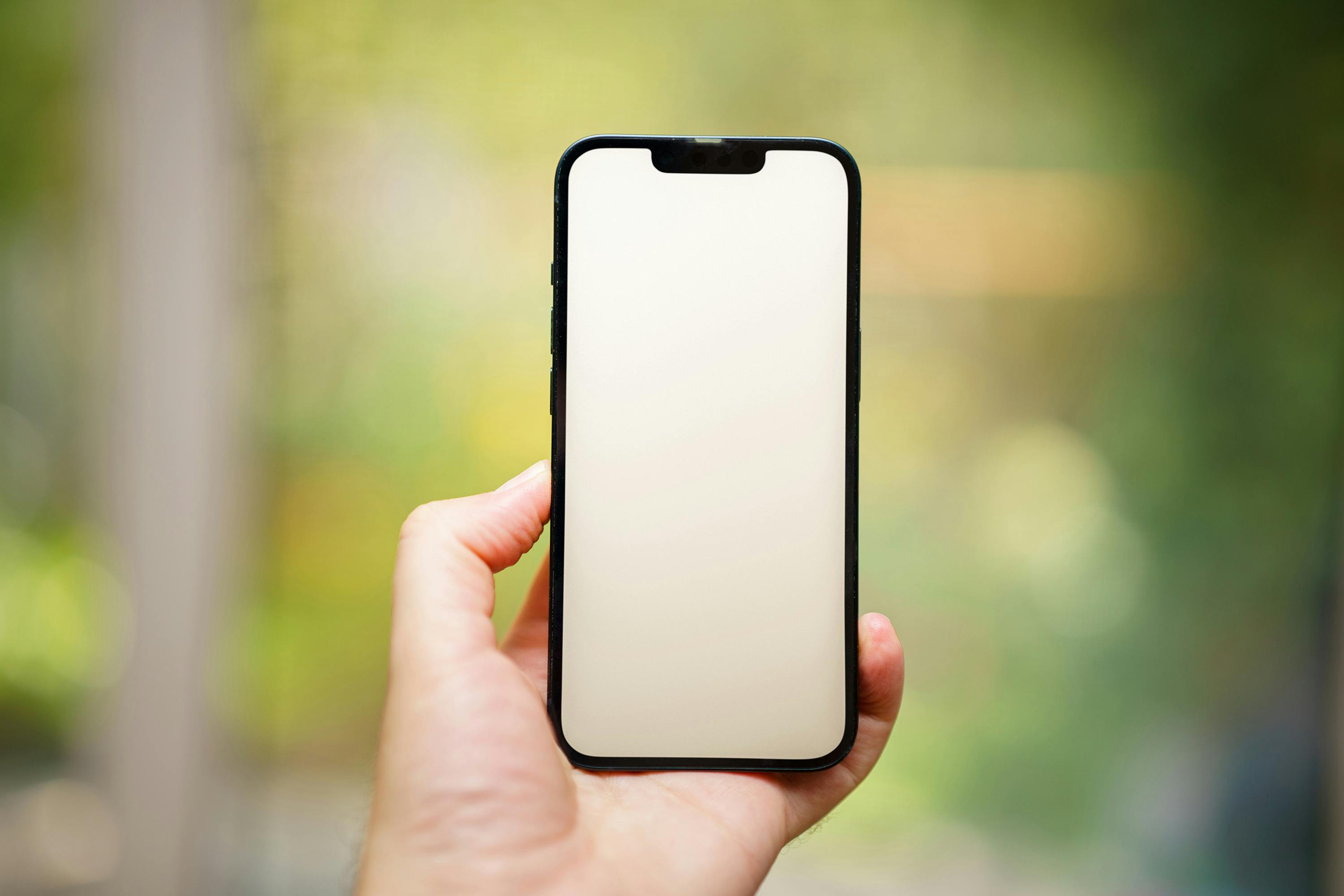 A hand holding a blank smartphone screen outdoors, ideal for mockups.