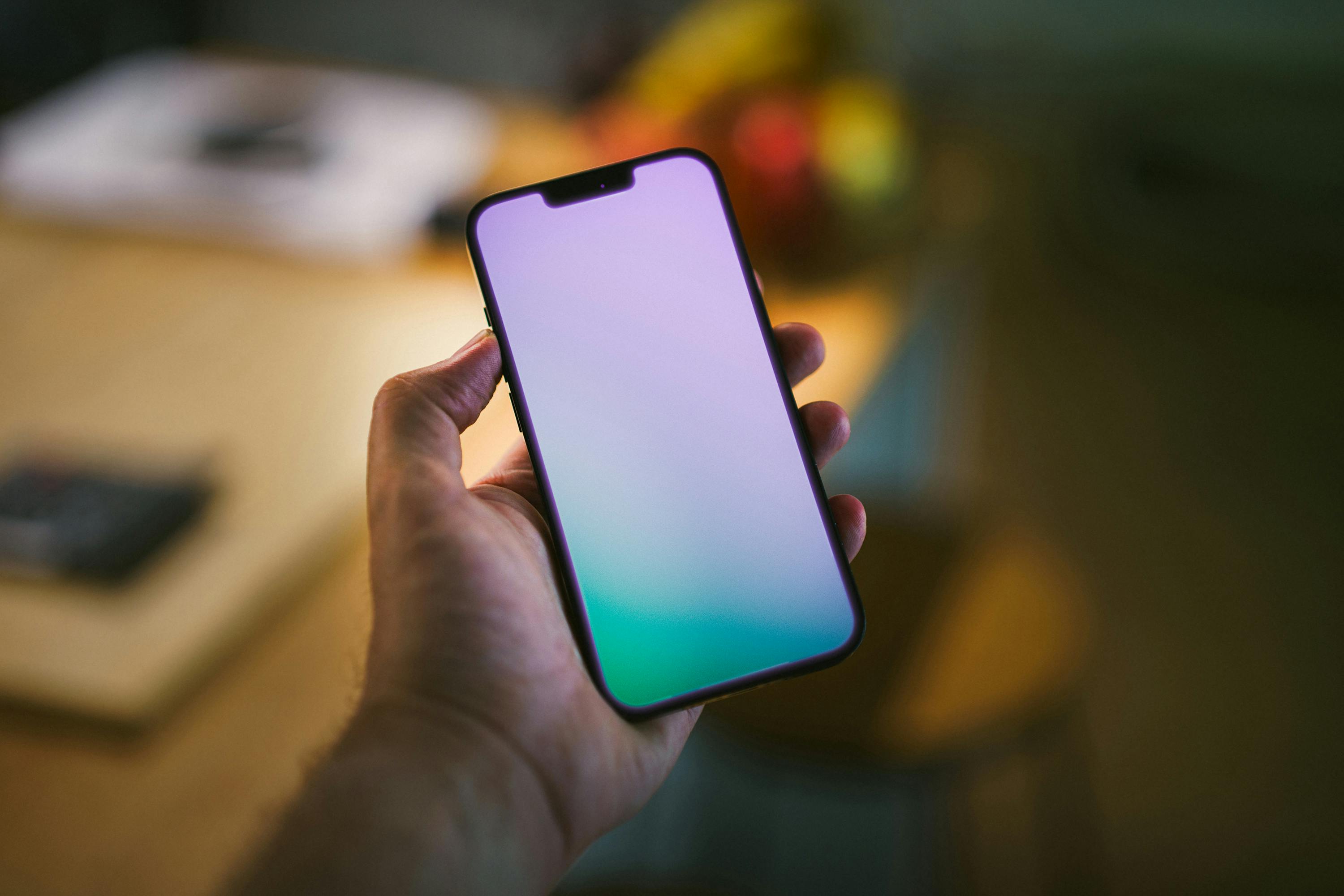 A close-up view of a hand holding a smartphone with a blank screen inside a home environment.