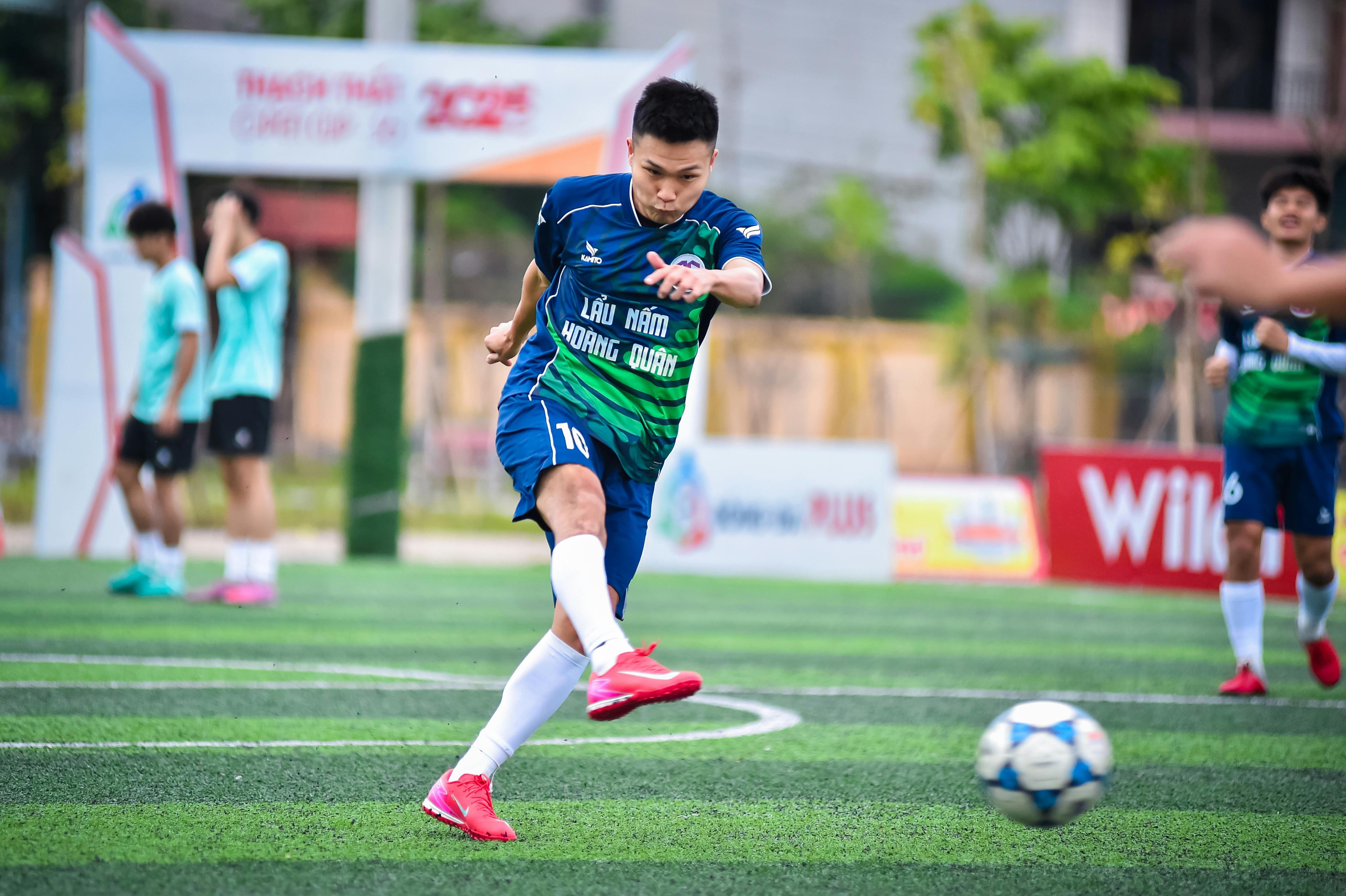 Athlete in action kicking a soccer ball on a Hanoi turf field during a daytime game.