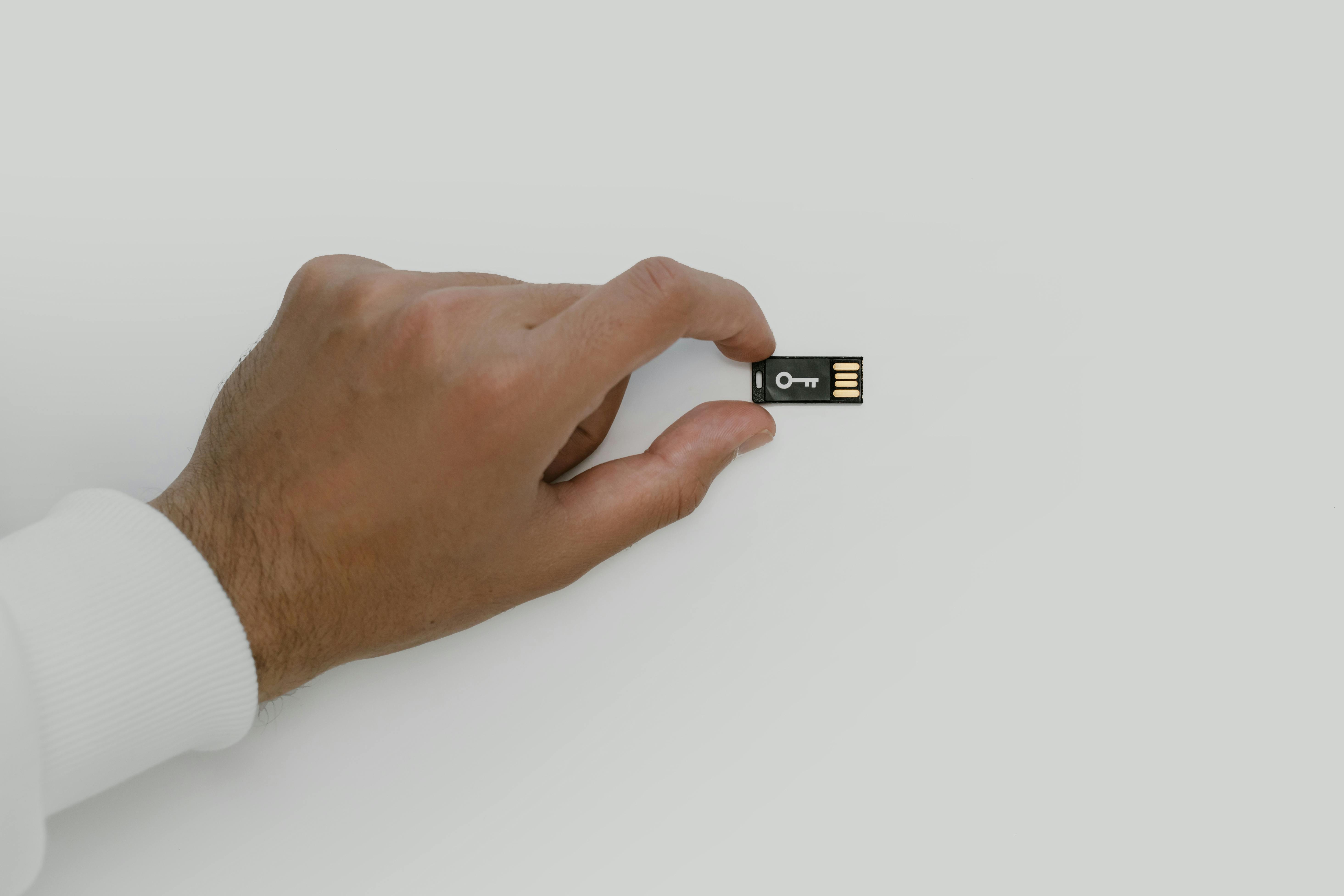 Close-up of a hand holding a USB flash drive with a key symbol, signifying digital security.