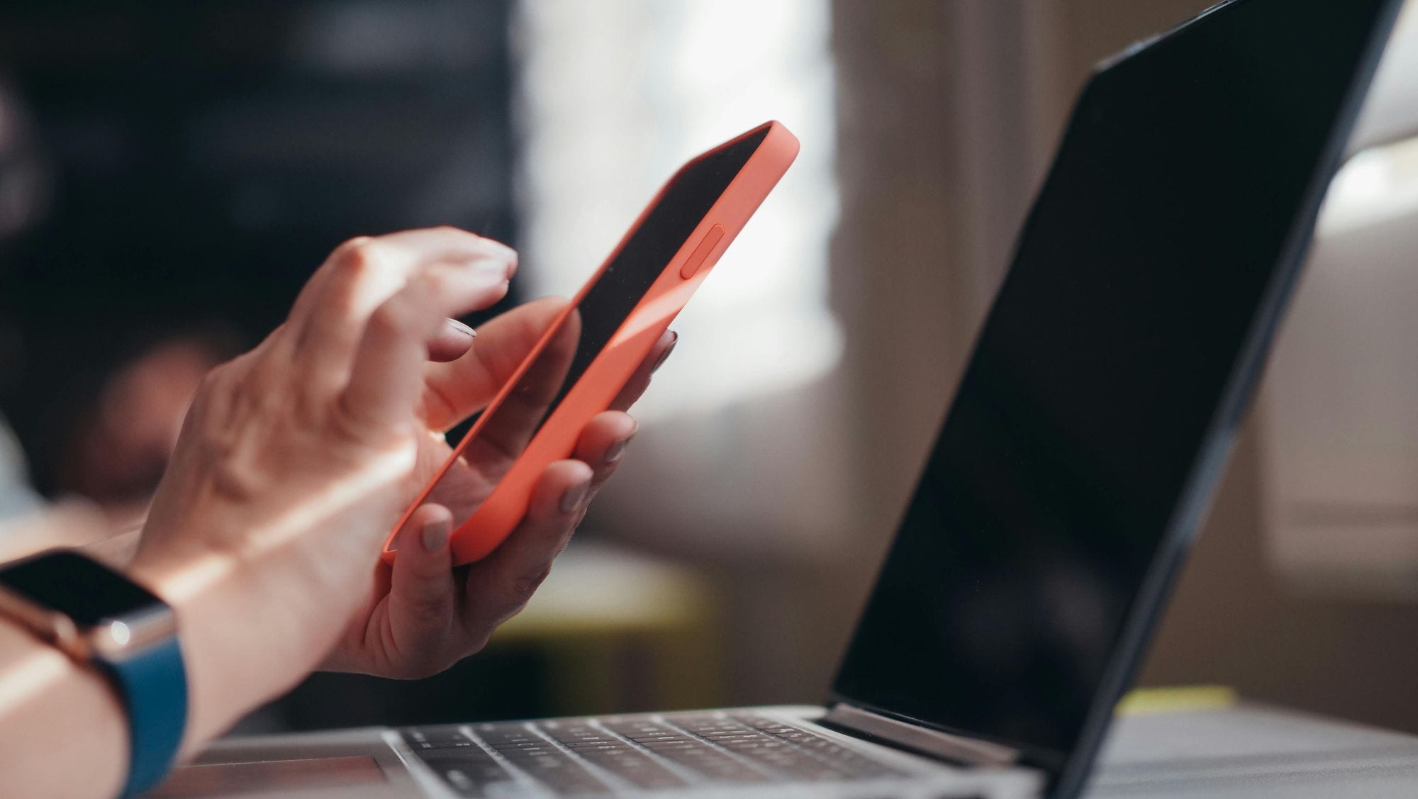 Adult using a smartphone and laptop indoors, showcasing modern technology and multitasking.